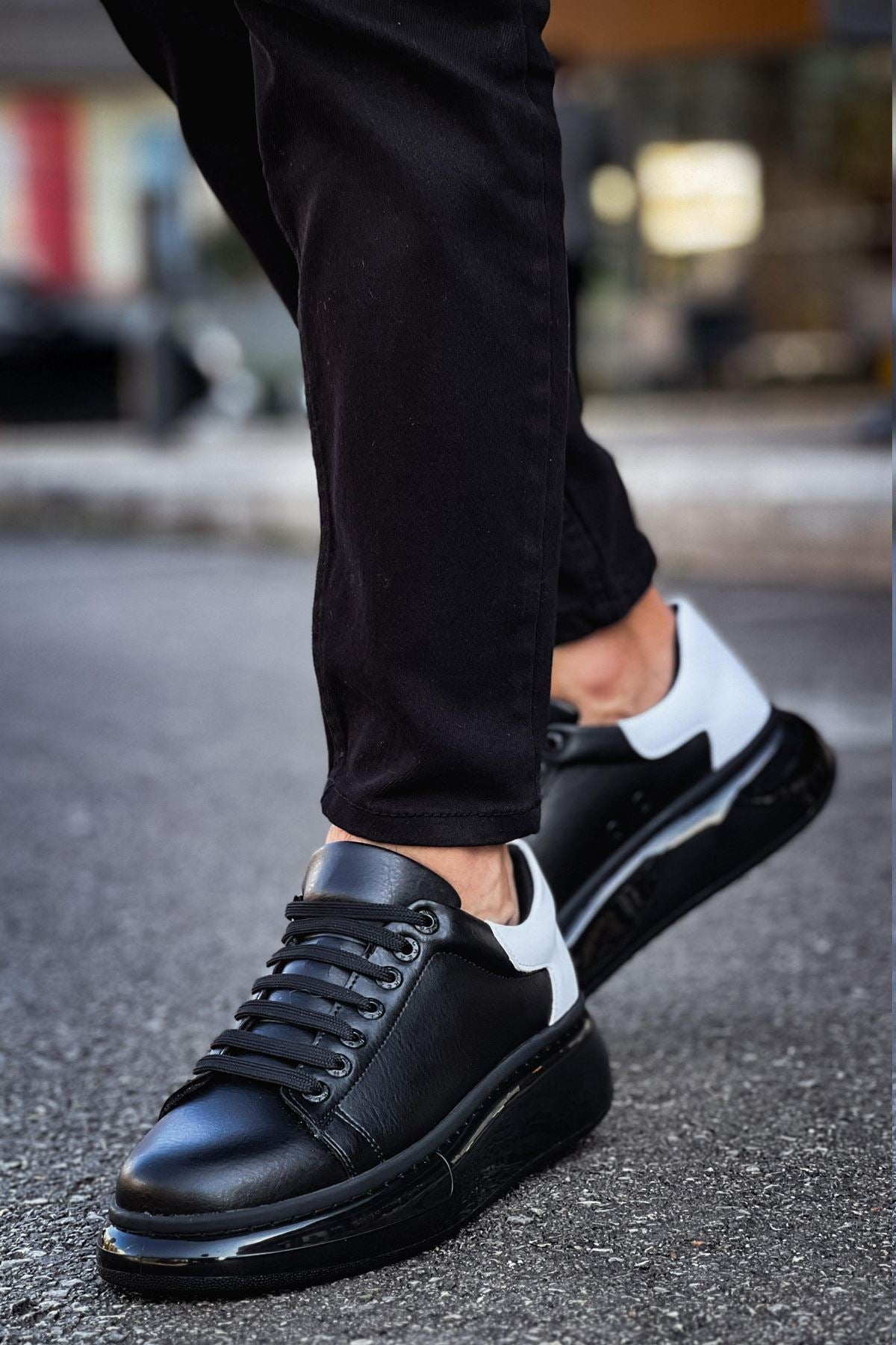 Black leather shoes with white soles worn by a person on a blurred street background