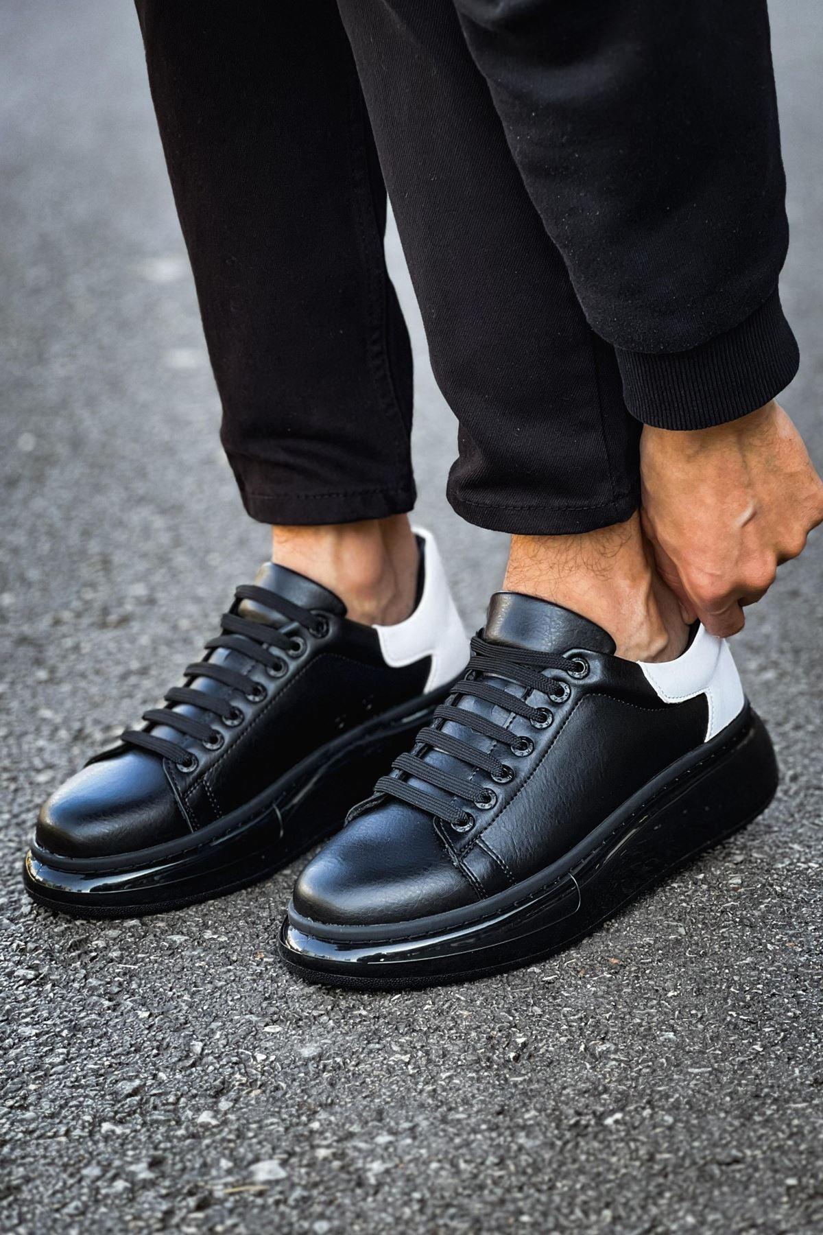Black leather sneakers worn with black pants on a gray pavement background