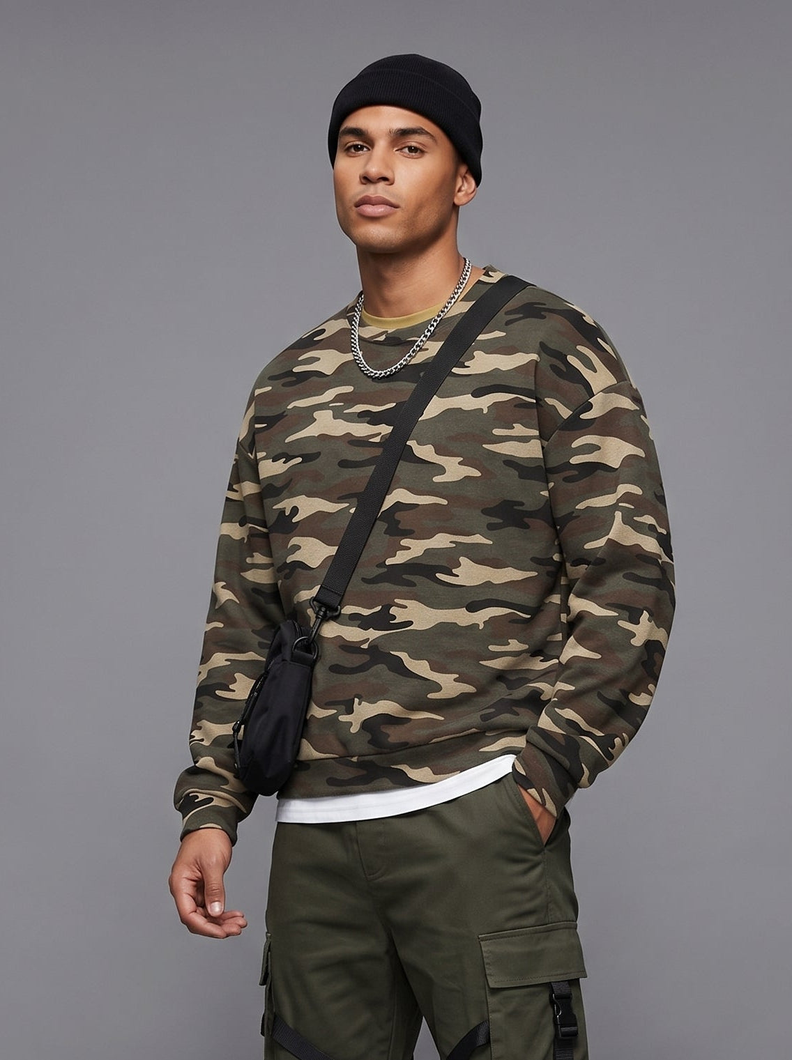 Man wearing a camouflage sweater and green cargo pants on a gray background