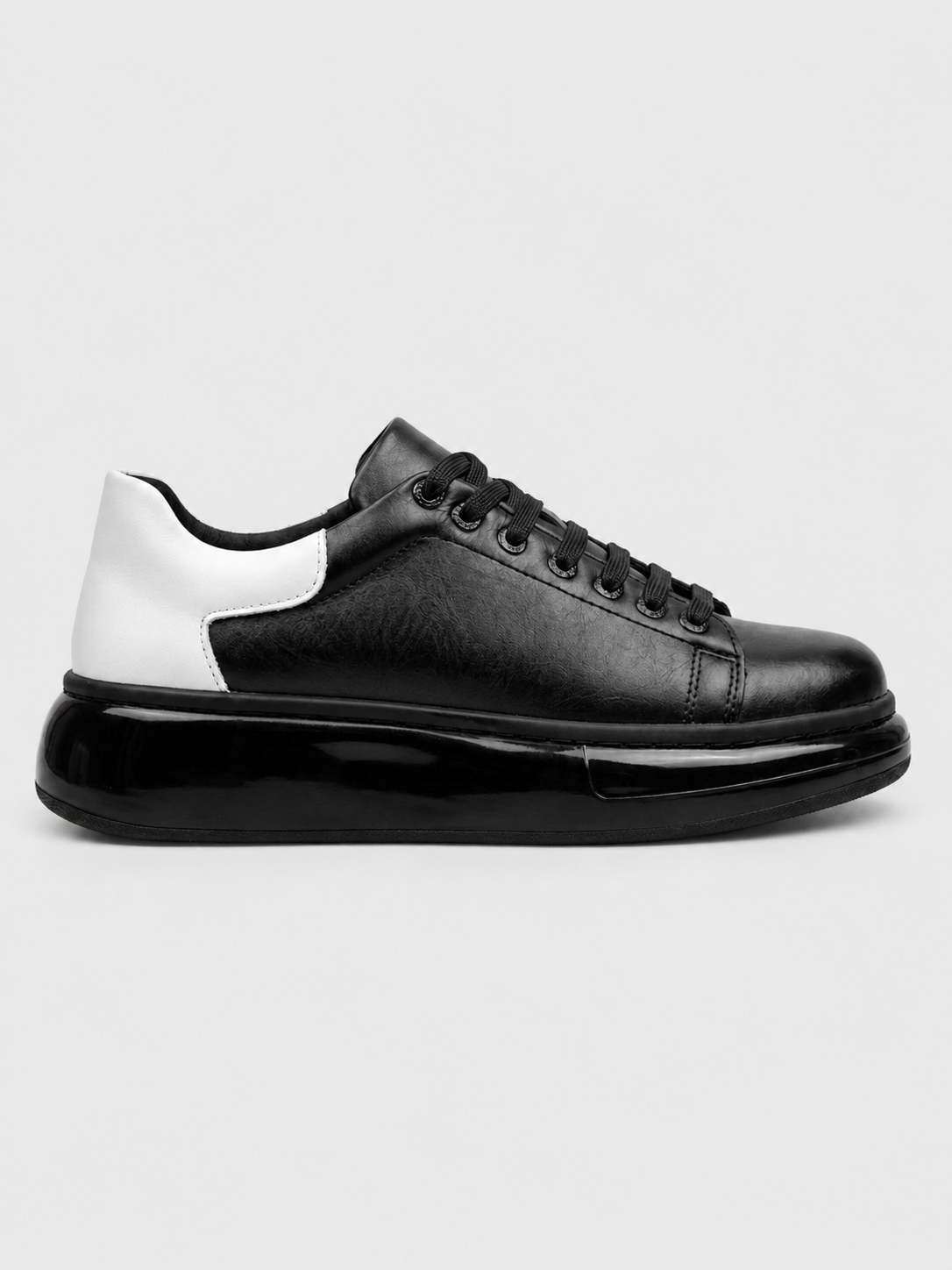 A black leather low-top sneaker with a chunky black platform sole and a contrasting white heel panel, shown in a side profile on a light gray background.