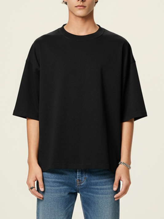 Person wearing a black oversized t-shirt and blue jeans on a beige background